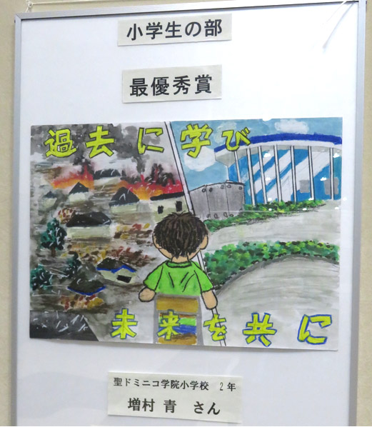 小学生の部最優秀賞に選ばれた小学2年生増村青さんの作品。大震災後に生まれた児童の作品で、当時の映像などで見聞きした被災の実態と整備された被災施設が「過去に学び未来を共に」の標語とともに描かれている